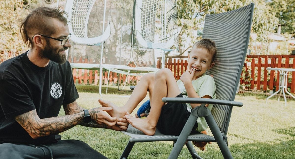 Playful interaction between a father and son in a sunny backyard setting.
