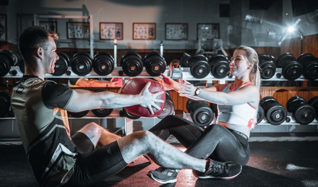A couple engaged in a fitness session using a medicine ball in a gym environment.