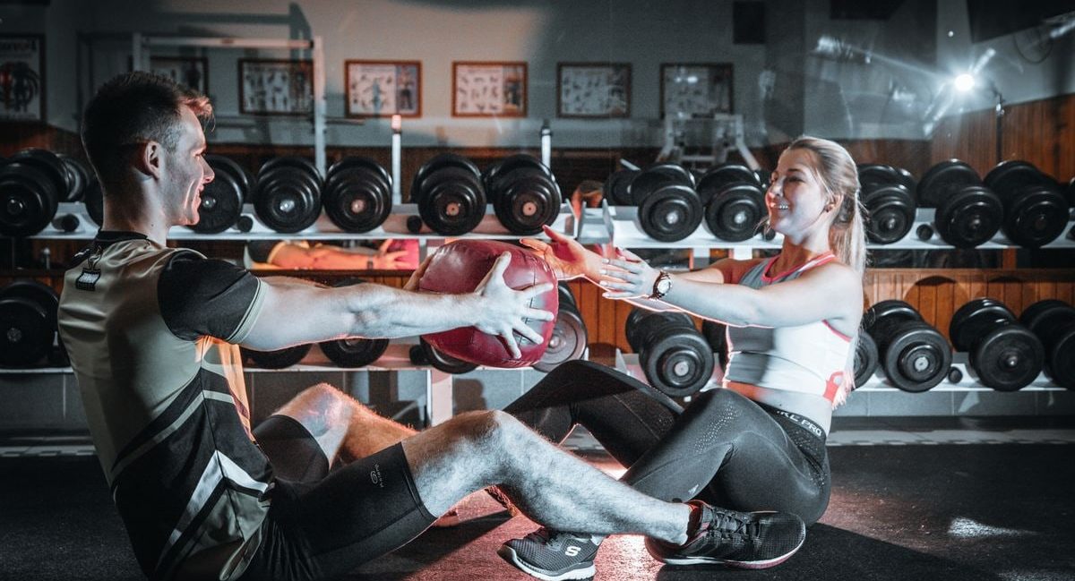 A couple engaged in a fitness session using a medicine ball in a gym environment.