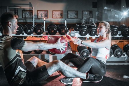 A couple engaged in a fitness session using a medicine ball in a gym environment.